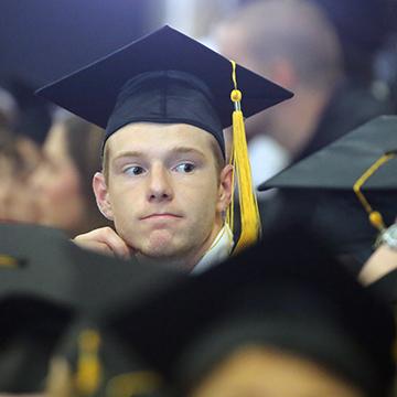 一名男子坐在GED毕业典礼上的毕业生中间.