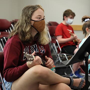 masked female student playing the ukulele